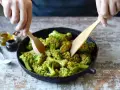 Broccoli in padella, condito con olio e spezie, viene mescolato con due palette di legno.