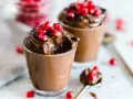 Due bicchierini di golosa mousse al cioccolato, guarniti con chicchi di melagrana e scaglie di cioccolato.