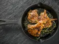 Tre succulenti costolette di agnello in padella, guarnite con rosmarino fresco, pronte per essere gustate.