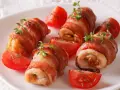Involtini di pollo avvolti in pancetta croccante, guarniti con timo fresco e serviti con spicchi di pomodoro.