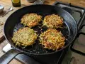 Quattro rosti di zucchine dorati e croccanti cuociono in padella, pronti per essere gustati.