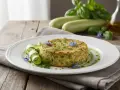 Delicato flan di zucchine, guarnito con fiori blu e rotolini di zucchina, su un piatto bianco.