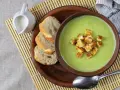 Una ciotola di cremosa crema di zucchine con crostini dorati, accompagnata da pane fresco e una caraffa di latte.