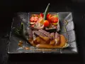 Straccetti di manzo succulenti su un piatto scuro, accompagnati da verdure miste e una salsa cremosa.