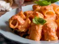Piatto di pasta ricotta e pomodorini, condita con una cremosa salsa e guarnita con foglie di basilico fresco.