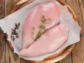 Due petti di pollo crudi, freschi e succulenti, adagiati su carta forno con pepe misto e rametti di timo.