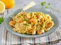 Un piatto di pasta con gamberetti, condita con limone e prezzemolo, accompagnata da limoni freschi e parmigiano.