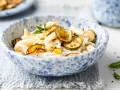 Piatto di pasta cremosa con ricotta e zucchine croccanti, guarnito con scorza di limone e menta.