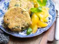 Hamburger di zucchine dorati e croccanti, serviti con pomodorini gialli e basilico fresco su un piatto blu e bianco.