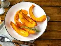 Fette di zucca al forno dorate e profumate, guarnite con rosmarino fresco, pronte per essere gustate.