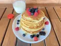 Pila di pancake senza zucchero guarnita con frutti di bosco freschi, accompagnata da un bicchiere di latte.