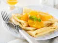 Deliziose crepes senza uova, guarnite con spicchi d'arancia succosa e foglioline di menta fresca. Un piatto leggero e gustoso.