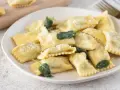 Piatto di ravioli del plin, dorati e spolverati di parmigiano, guarniti con foglie di salvia fresca.