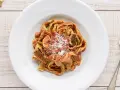 Un piatto di tagliatelle ai funghi, condite con sugo rosso e parmigiano grattugiato, su un tavolo di legno.