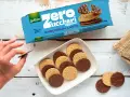 Biscotti senza zucchero Gullón Chocoslim Latte, alcuni ricoperti di cioccolato, su un piatto bianco. Una mano ne prende uno.