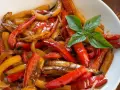 Peperoni in agrodolce, colorati e succosi, guarniti con basilico fresco. Un contorno saporito e invitante.