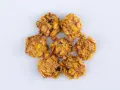 Biscotti croccanti, simili a rose del deserto, con fiocchi di mais e uvetta, disposti a cerchio su sfondo bianco.