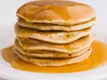 Pila di pancake dorati, inzuppati di sciroppo d'acero. Perfetti per una ricetta pancake proteici sana e golosa.