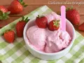 Una ciotola di cremoso gelato alla fragola, guarnito con fragole fresche, su una tovaglietta a quadri verdi.