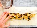 Mani che preparano uno strudel di mele con pasta sfoglia, riempiendolo con mele a cubetti, uvetta e pinoli.