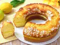 Un soffice ciambellone al limone, decorato con perline di zucchero, con una fetta tagliata che rivela un ripieno cremoso.