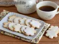 Biscotti con farina di riso a forma di fiore, spolverati di zucchero a velo, accanto a una tazza di tè e una teiera.