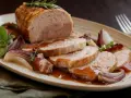 Un succulento arrosto di tacchino affettato, servito con cipolle rosse caramellate e salsa bruna su un piatto rustico.