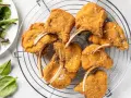 Deliziose costolette d'agnello fritte, dorate e croccanti, cosparse di sale grosso, su una griglia. Accanto, un'insalata fresca.