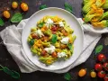 Piatto di pasta con crema di zucchine, pomodorini confit, fiori di zucca e ricotta fresca. Un tripudio di sapori estivi.