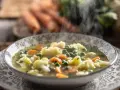 Zuppa fumante con cavolfiore, piselli e carote, arricchita da un tocco di panna da cucina per una cremosità avvolgente.