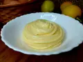 Una spirale di soffice crema al limone in una ciotola bianca, con limoni e uova sullo sfondo.