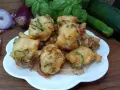 Frittelle di zucchine dorate e croccanti, pronte per essere gustate. Sullo sfondo, cipolle rosse, basilico fresco e zucchine.