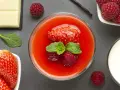 Delizioso coulis di fragole guarnito con fragola, lamponi e menta. Accanto, cioccolato bianco, lamponi freschi e un bicchiere di latte.