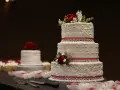 Torta nuziale a tre piani decorata con pasta di zucchero, rose rosse e nastri scintillanti. Cupcake e un'altra torta sullo sfondo.