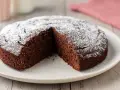 Una fetta è stata tolta da questa torta al cioccolato morbida, cosparsa di zucchero a velo.