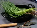 Mazzo di agretti freschi con radici, pronti per essere cotti in padella. Un coltello è appoggiato accanto.