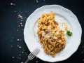 Un piatto di risotto funghi e salsiccia, guarnito con parmigiano grattugiato e prezzemolo, pronto per essere gustato.