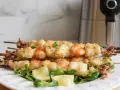 Spiedini di gamberi e calamari dorati e croccanti, cotti alla perfezione nella friggitrice ad aria. Serviti su un letto di insalata con spicchi di limone.