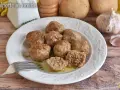 Piatto di polpette in bianco, morbide e succulente, pronte per essere gustate. Sullo sfondo patate e aglio.