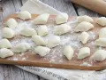 Gnocchi di ricotta freschi, pronti per essere cotti, spolverati di farina su un tagliere di legno.