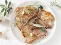 Tre succulente braciole di maiale cotte alla perfezione, guarnite con aglio, rosmarino e salvia.