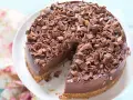 Cheesecake alla Nutella golosa, ricoperta di riccioli di cioccolato fondente. Una fetta è già stata servita, invitando a gustarla.