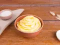 Una ciotola piena di soffice crema al burro, pronta per decorare torte. Accanto, ciotoline con zucchero e decorazioni naturali.