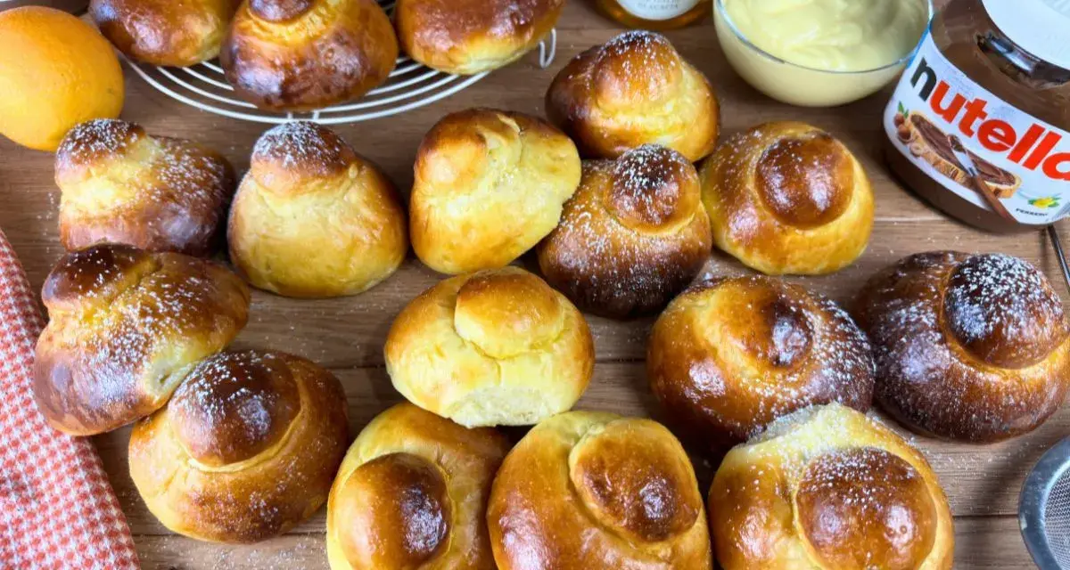 Tanti brioche col tuppo dorati, alcuni spolverati di zucchero a velo, pronti per essere farciti con crema o Nutella.
