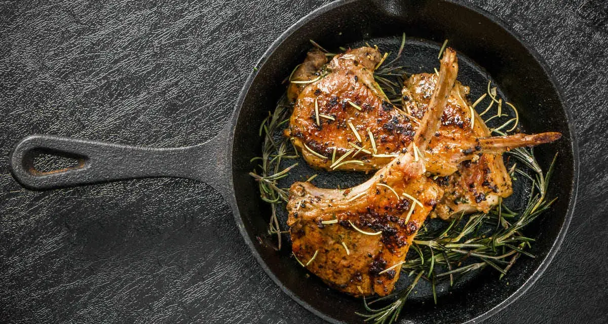 Tre succulenti costolette di agnello in padella, guarnite con rosmarino fresco, pronte per essere gustate.