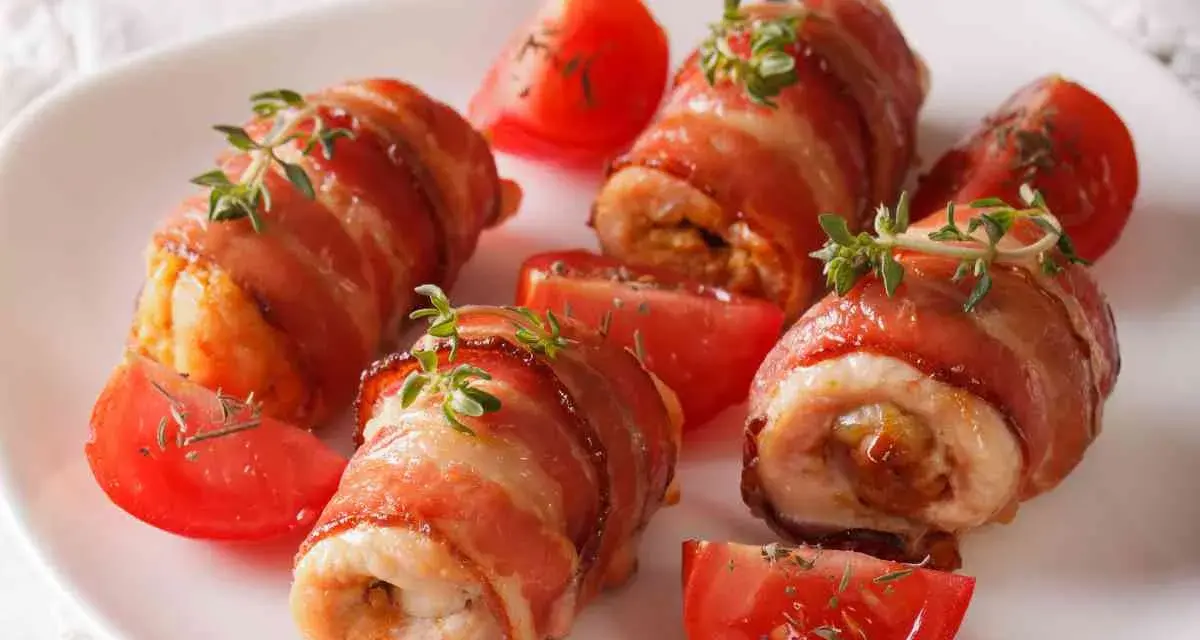Involtini di pollo avvolti in pancetta croccante, guarniti con timo fresco e serviti con spicchi di pomodoro.