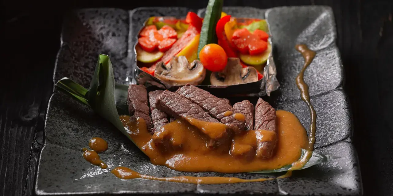 Straccetti di manzo succulenti su un piatto scuro, accompagnati da verdure miste e una salsa cremosa.