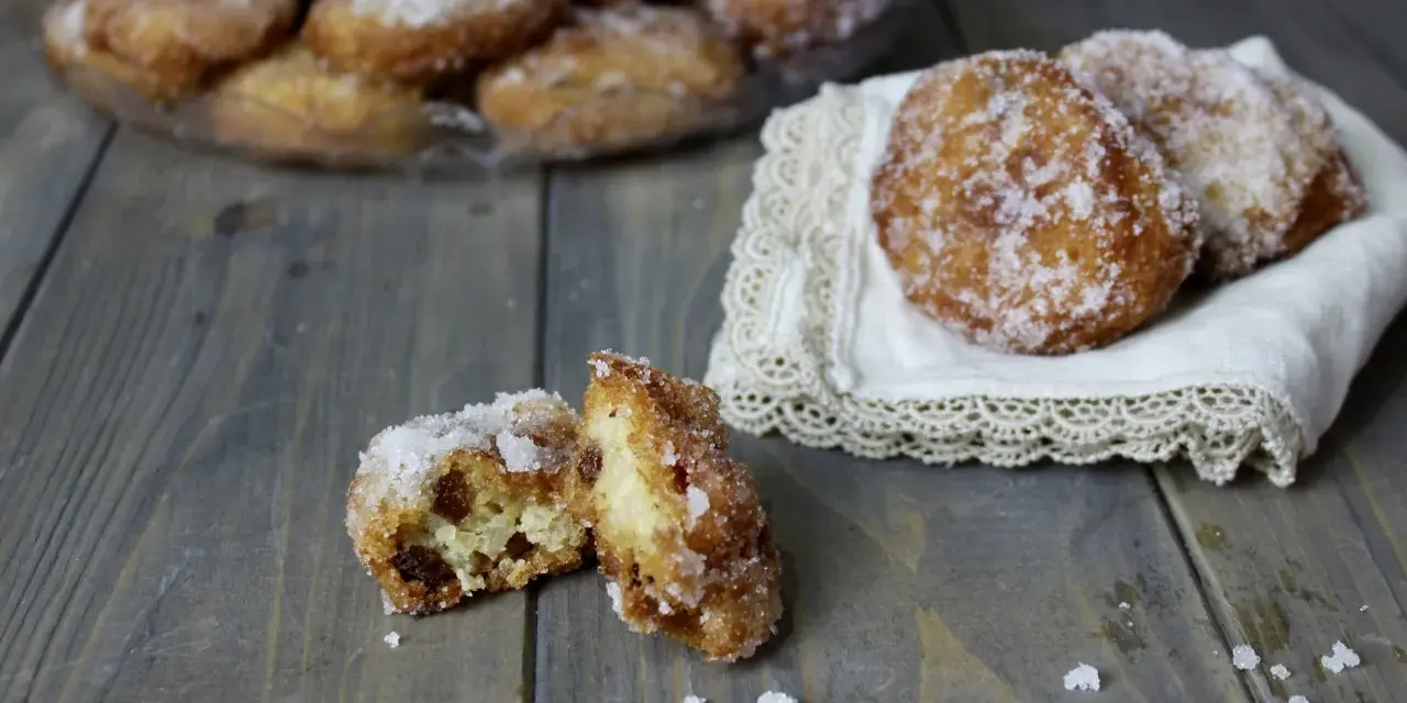 Frittelle di riso ricetta della nonna: dolcetti dorati e zuccherati, uno aperto rivela l'interno soffice e i chicchi d'uva passa.
