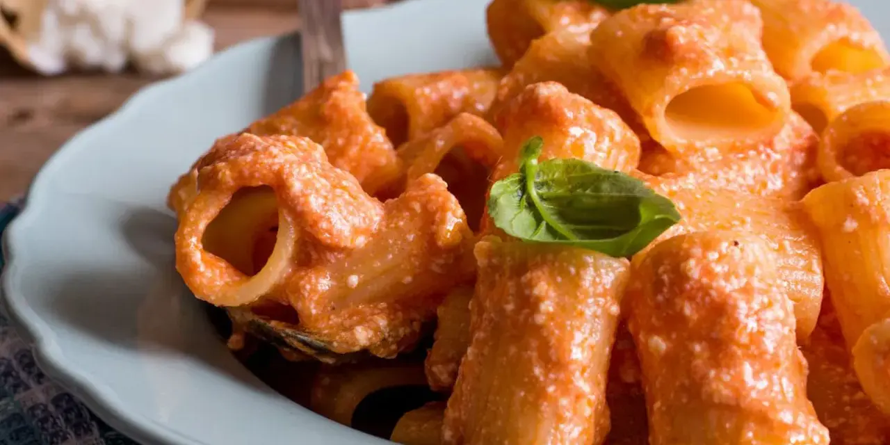 Piatto di pasta ricotta e pomodorini, condita con una cremosa salsa e guarnita con foglie di basilico fresco.
