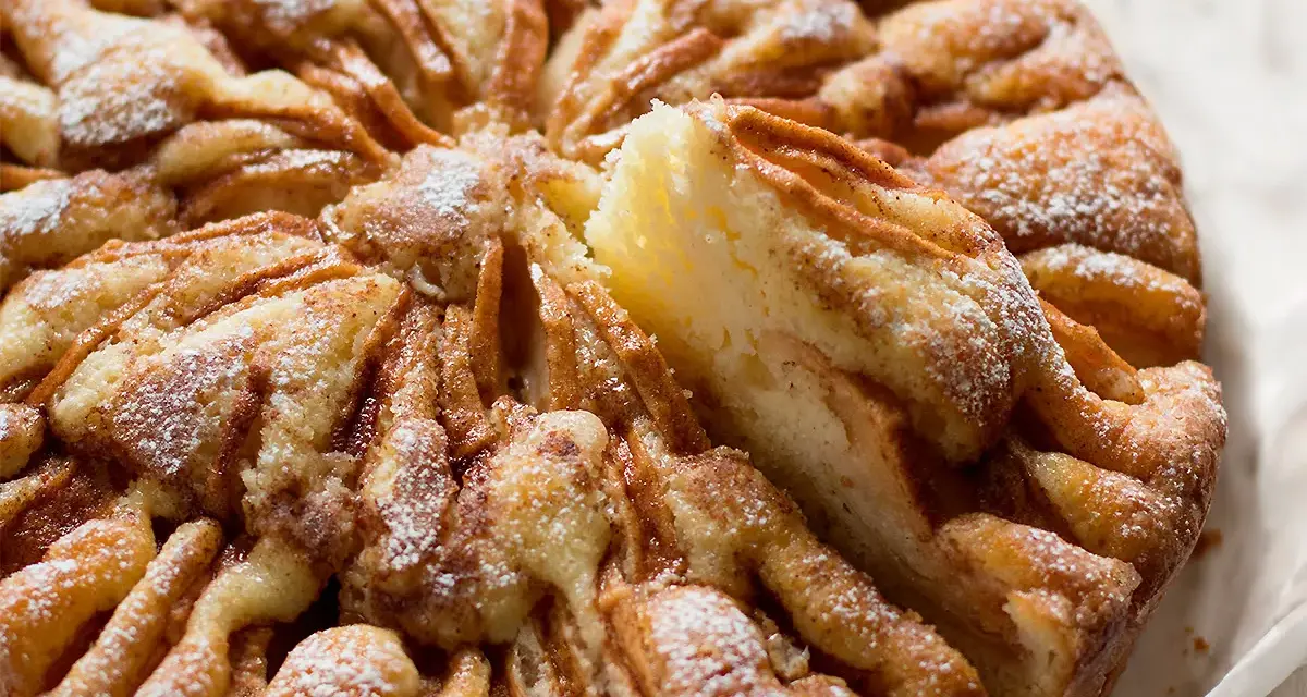 Una deliziosa torta di mele, cosparsa di zucchero a velo, con una fetta sollevata che rivela la morbida consistenza.